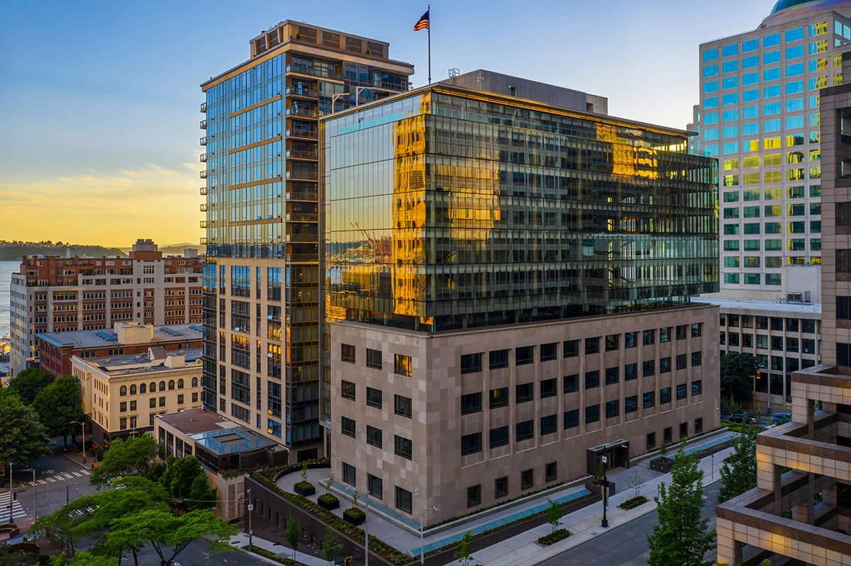 The Reserve Building at 1015 Second Avenue in Seattle featuring beige stone podium base and glass upper floors at sunset with Elliott Bay in background
